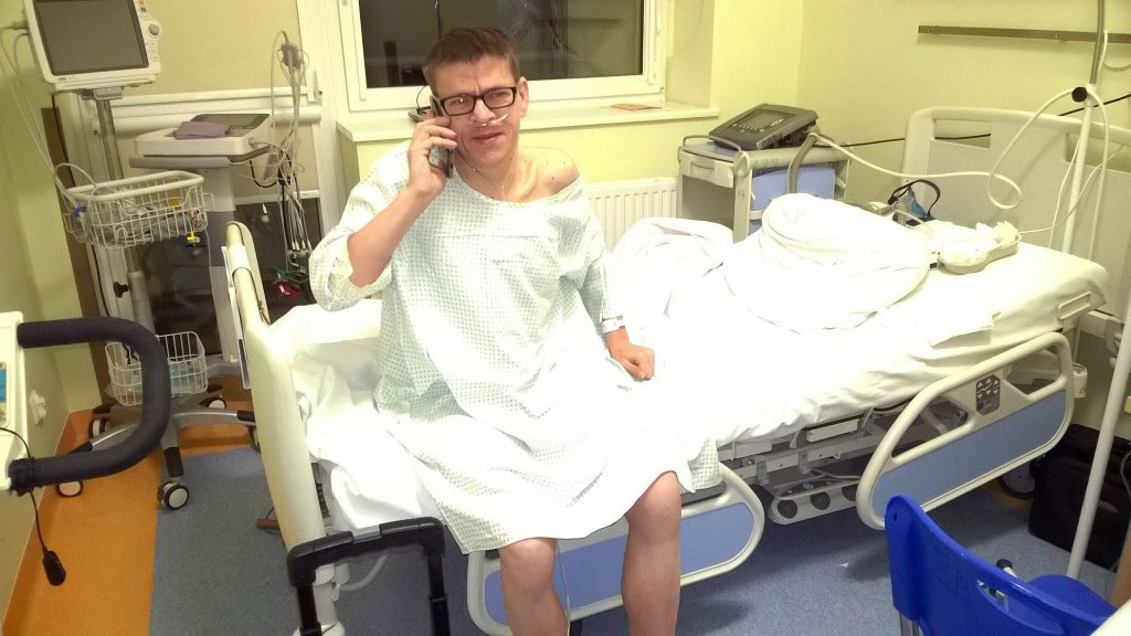 Rafał siedzący na łóżku szpitalnym rozmawia przez telefon