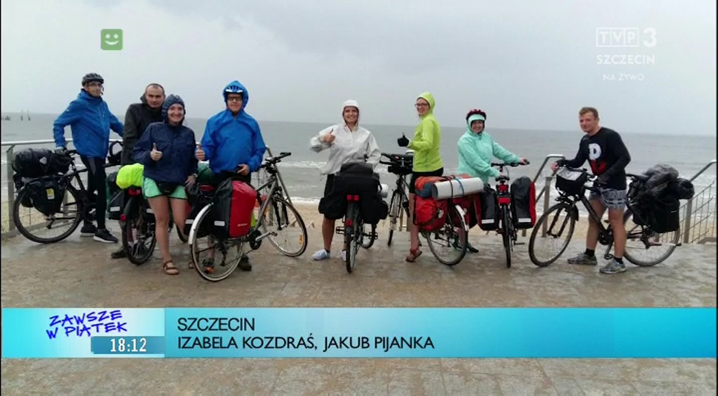 Grupa rowerzystów w kurtkach przeciw deszczowych na tle morza