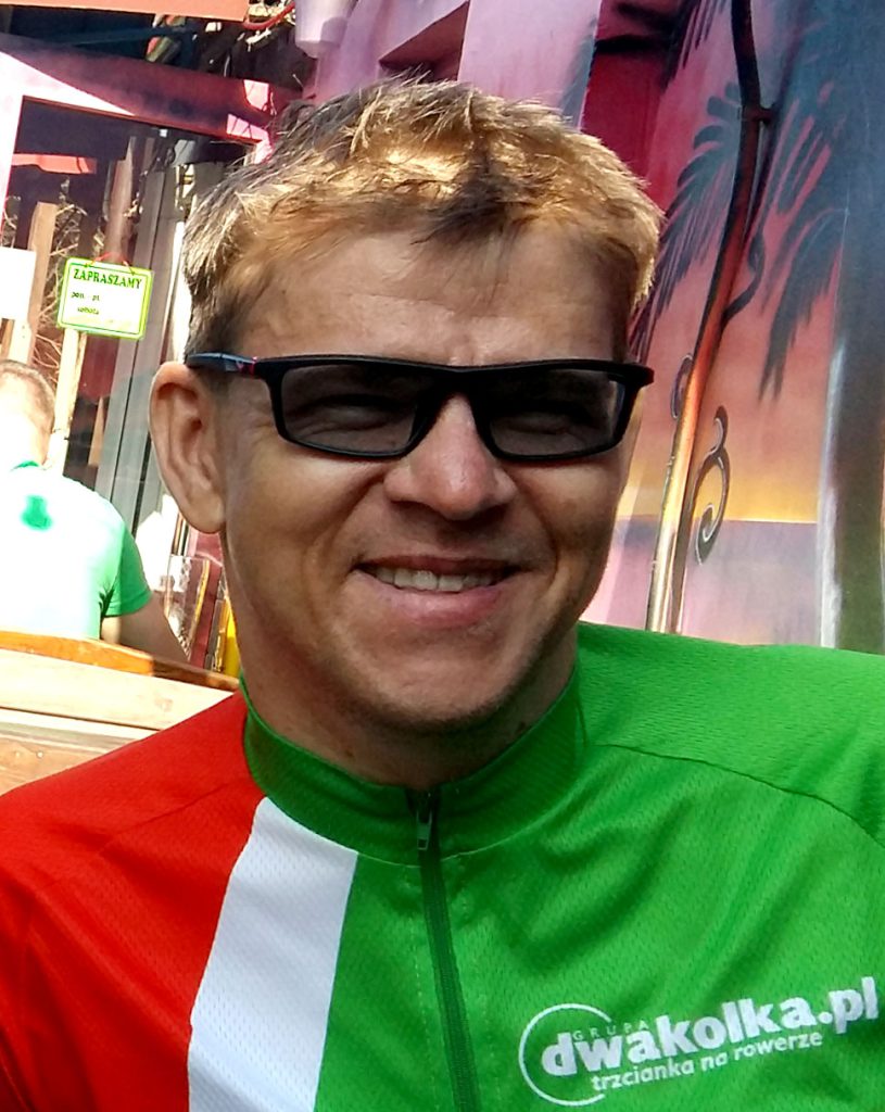Uśmiechnięty Rafał w koszulce rowerowej grupy dwakolka.pl w kolorze czerwono biało zielonym